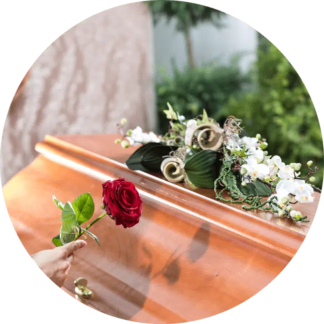 A circular cropped image of a coffin with flowers and a had placing a rose.